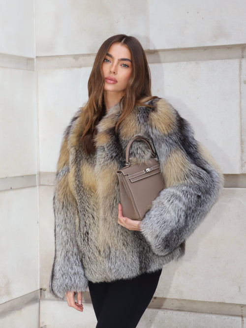Grey and golden fox fur coat styled with black trousers and handbag, showing oversized silhouette and natural fur texture.