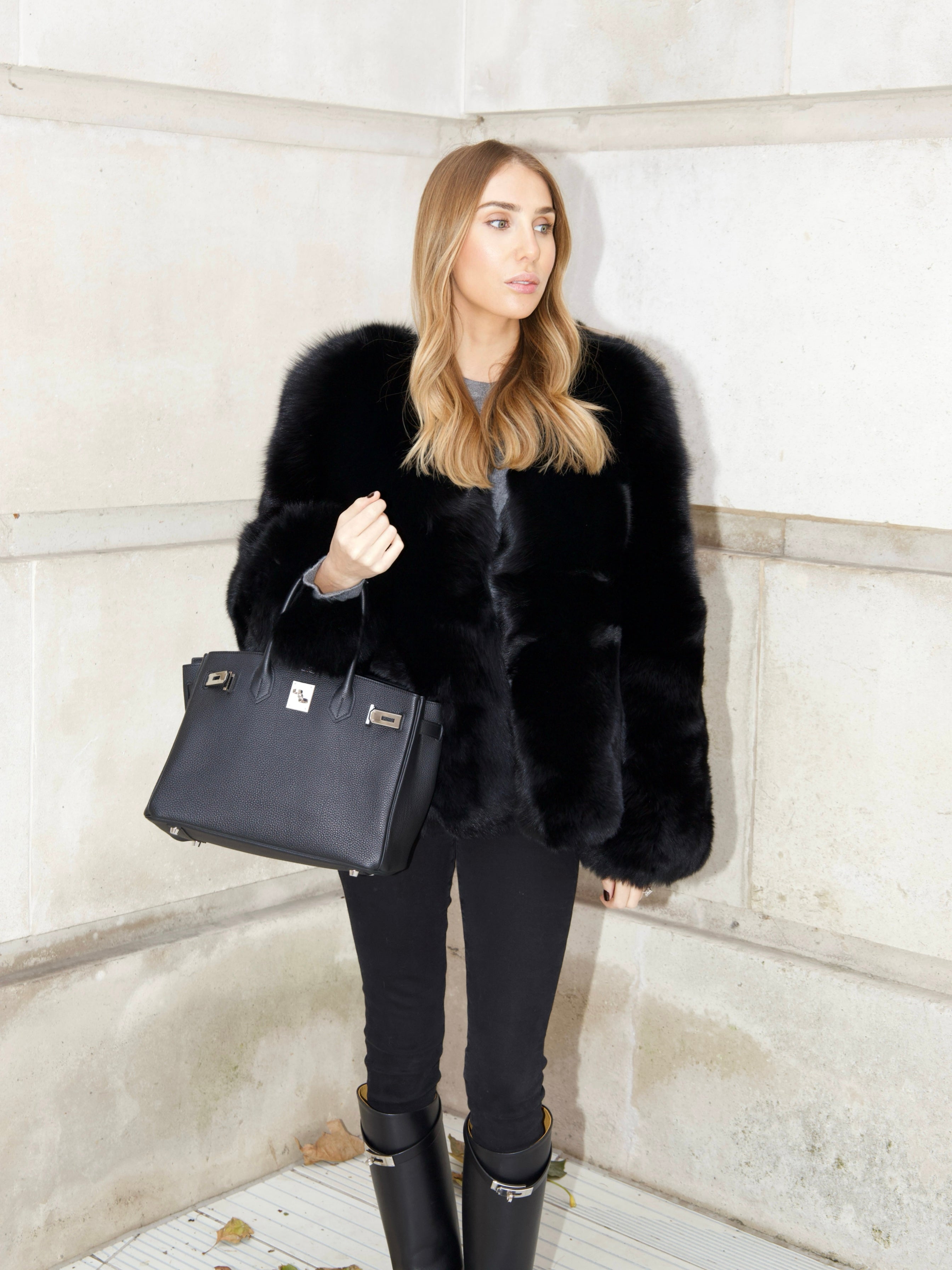 Full length look of The Anouska Fox Fur Coat in black styled with black trousers, boots and a handbag