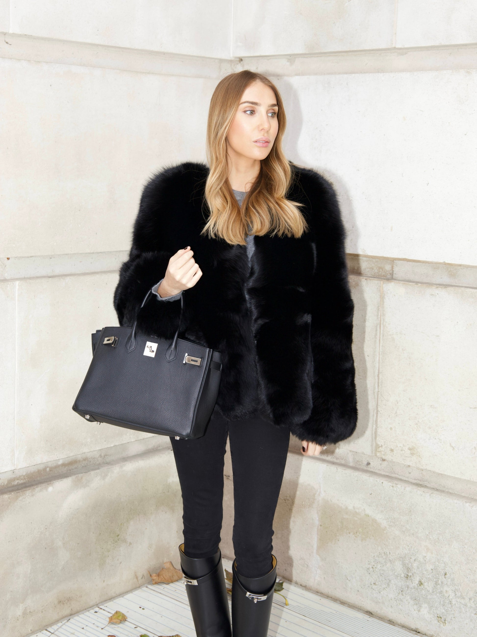 Full length look of The Anouska Fox Fur Coat in black styled with black trousers, boots and a handbag